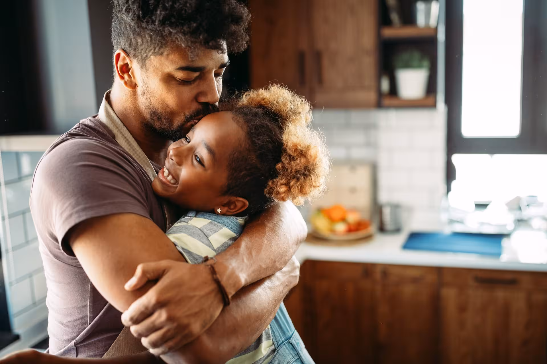 father hugging his young daughter and kissing her forehead