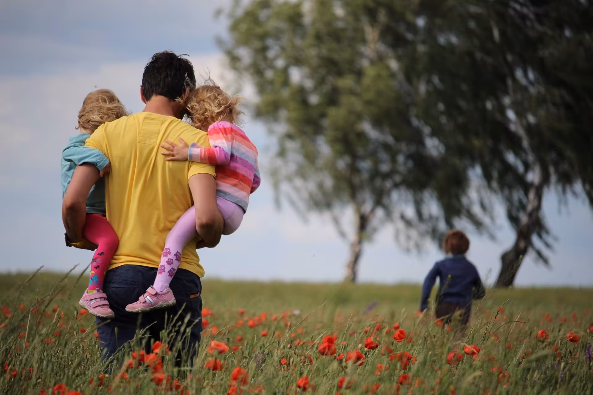 Father carrying his two daughters in a field of flowers